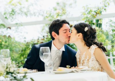 Gli sposi si baciano al tavolo nella sala del ricevimento di matrimonio a Relais Cascina Spiga D'Oro