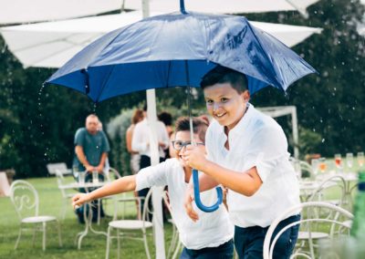 Due bambini corrono sotto la pioggia con l'ombrello durante il ricevimento di matrimonio a Villa Rosantica